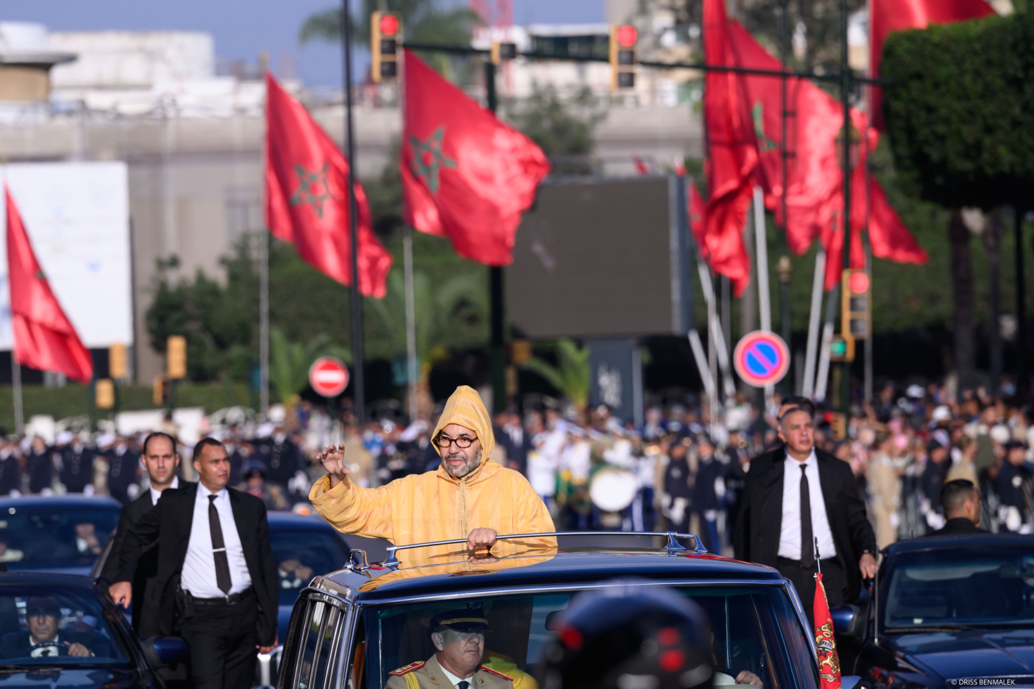 Le Roi Mohammed VI saluant la foule à l'occasion de l'ouverture de la 12e Législature, sous les drapeaux marocains.